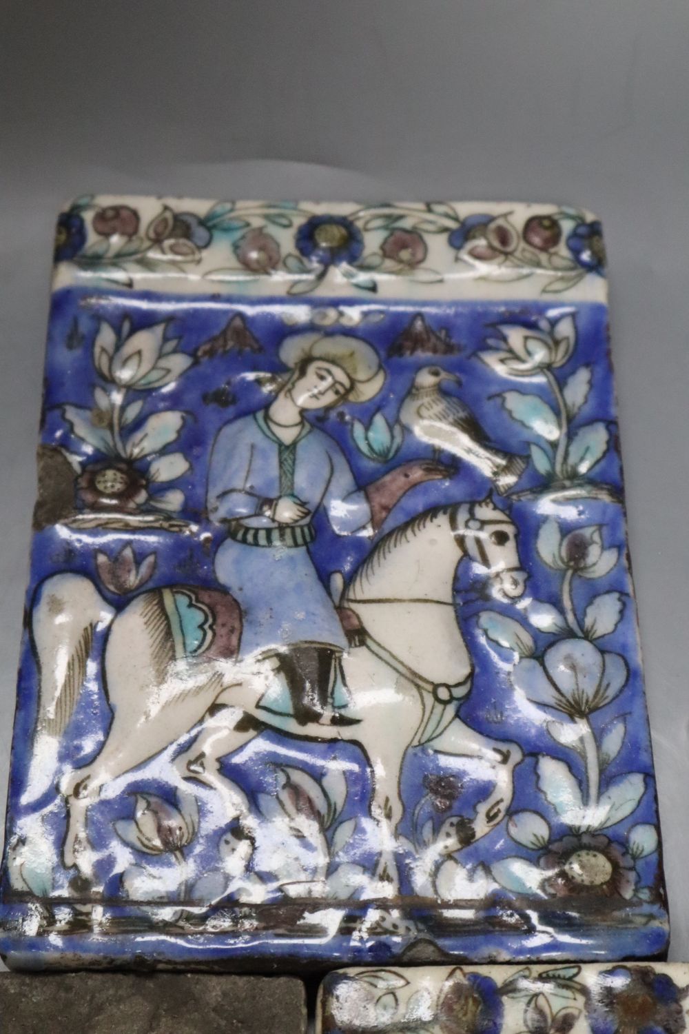 Three Persian pottery wall tiles, Qajar dynasty, relief-moulded with falconers on horseback, each approx 19 x 12.5cm